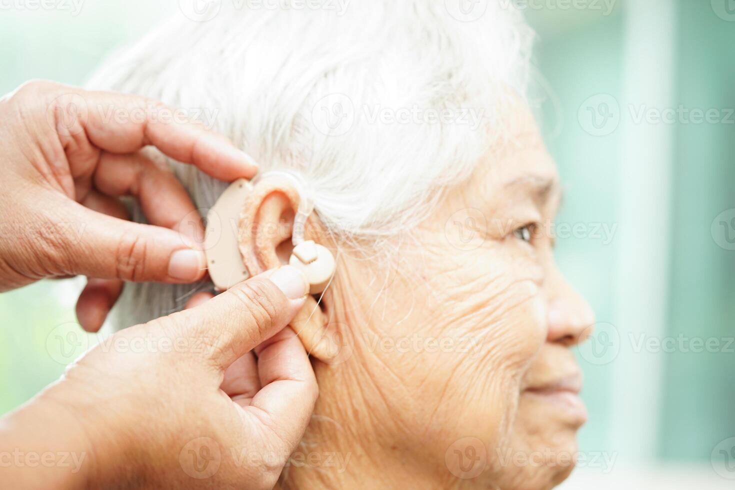 Doctor install hearing aid on senior patient ear to reduce hearing loss problem. photo