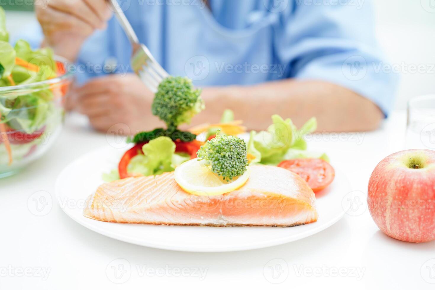 Asian elderly woman patient eating salmon stake and vegetable salad for healthy food in hospital. photo