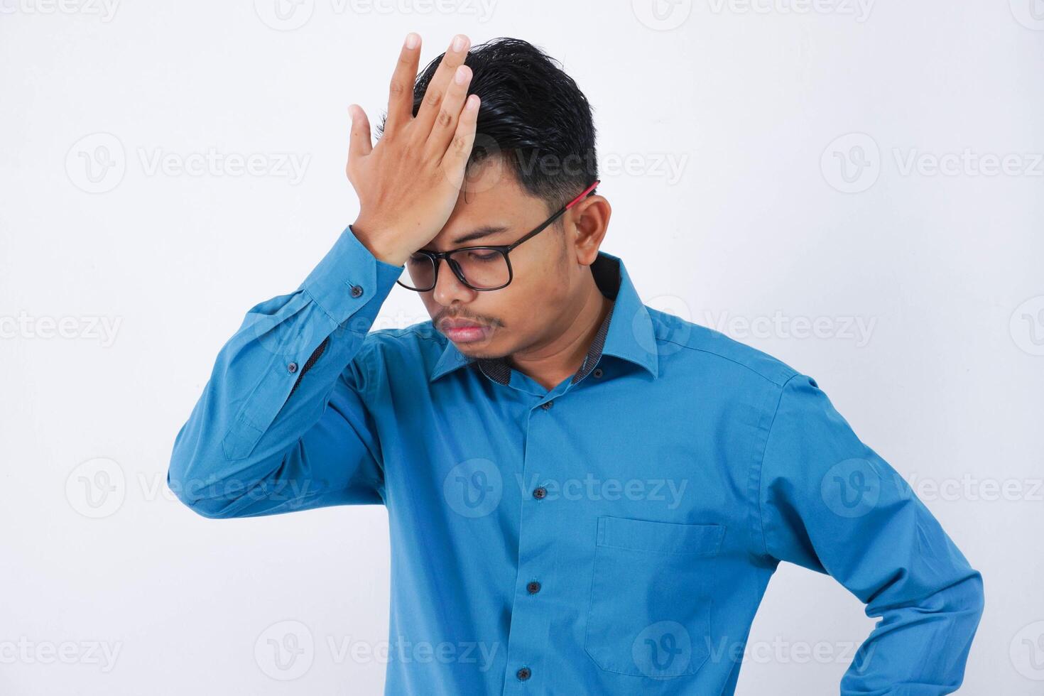 Handsome young asian businessman with glasses in wearing blue shirt forgetting something, slapping forehead with palm isolated on white background photo