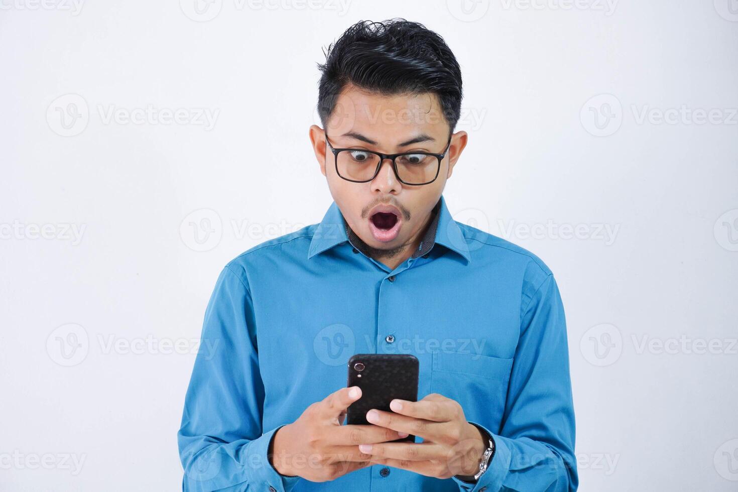 Portrait of surprised and shocked handsome young asian businessman with glasses in wearing blue shirt using smartphone isolated on white background photo