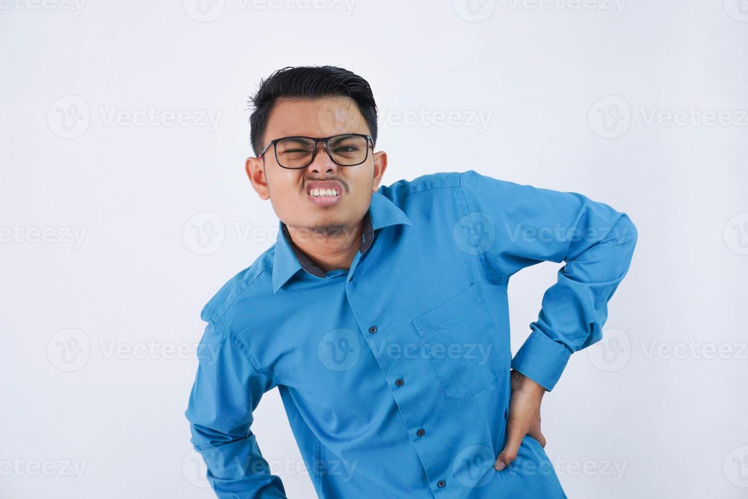 young asian man with glasses holding his waist in pain tired from work wearing blue shirt isolated white background photo