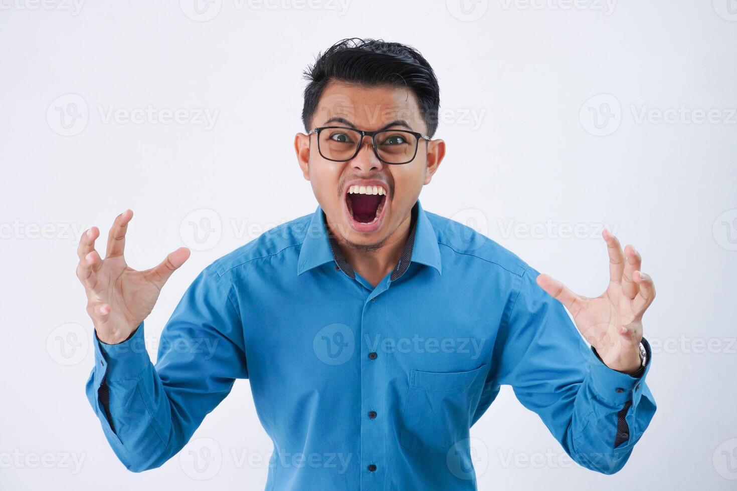 Annoyed handsome young asian man with glasses in wearing blue shirt raises palms while shouting loudly isolated on white background photo