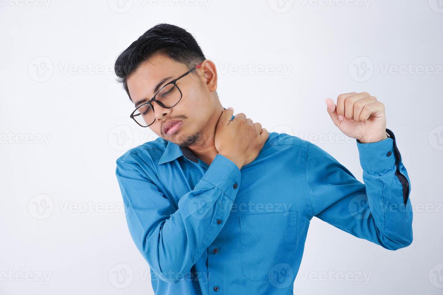 young asian man with glasses holding shoulder because tired of work feeling pain wearing blue shirt isolated on white background photo