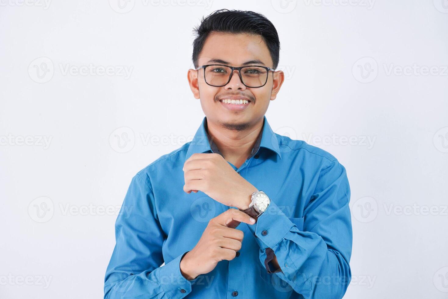 retrato joven asiático empleado hombre con lentes participación un reloj sonrisa y mirando cámara vistiendo azul camisa aislado en blanco antecedentes foto