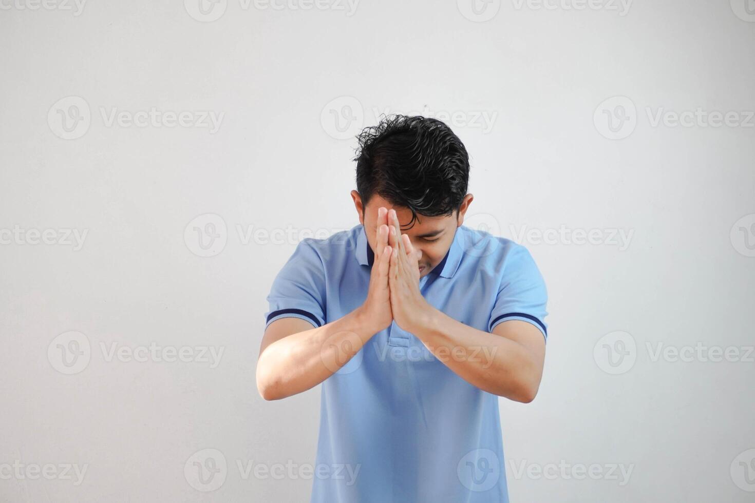 Young asian man wearing casual blue t shirt over white background begging with hands together with hope expression on face very emotional and worried. begging. sad face photo