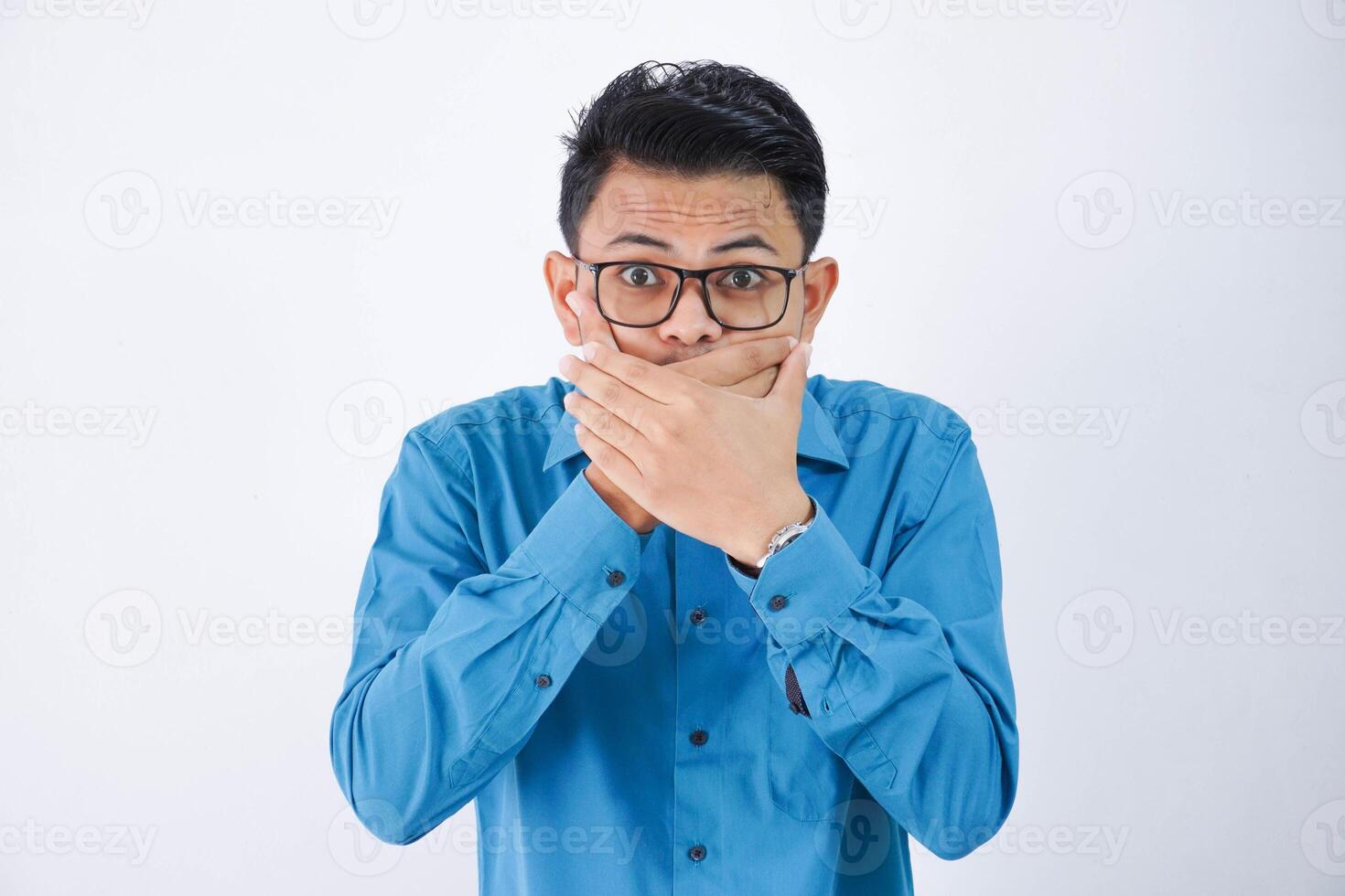 asian businessman covered his mouth with both hands with glasses wearing blue shirt isolated on white background photo
