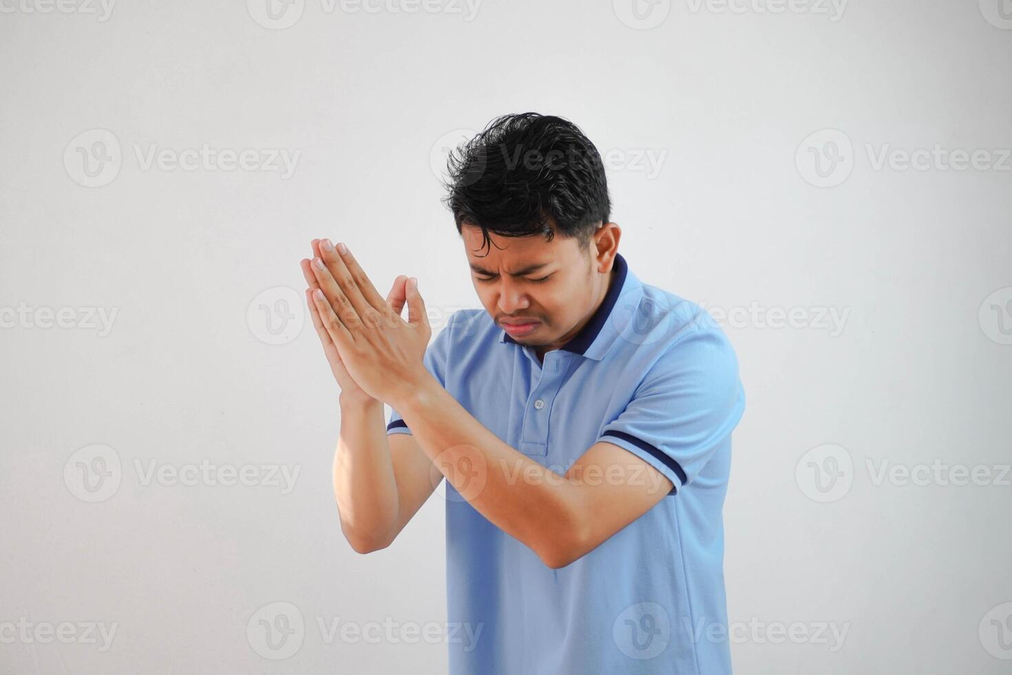 Young asian man wearing casual blue t shirt over white background begging with hands together with hope expression on face very emotional and worried. begging. sad face photo