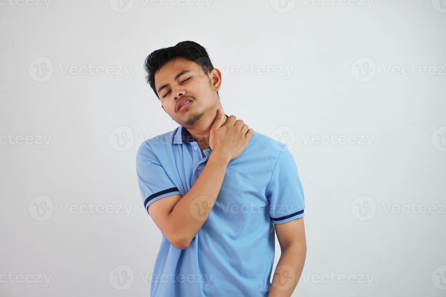 un retrato de joven asiático hombre teniendo tiene cuello y hombro dolor vistiendo azul t camisa aislado en blanco antecedentes foto