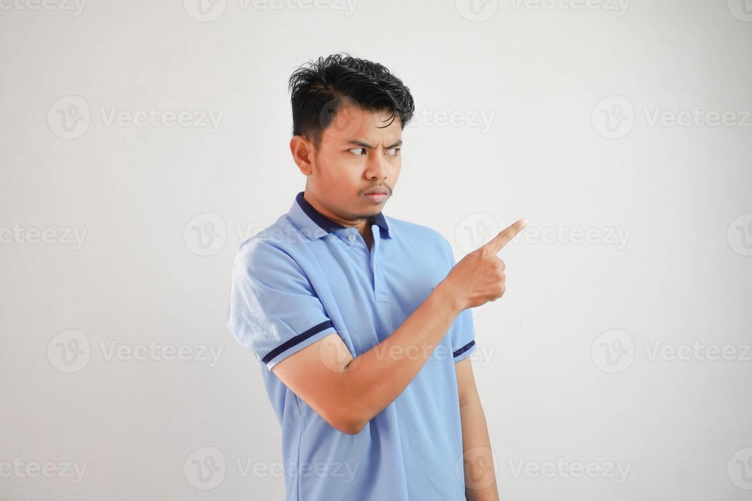 retrato de un pensativo joven asiático hombre con dedos señalando oblicuo vistiendo azul t camisa aislado en blanco antecedentes foto