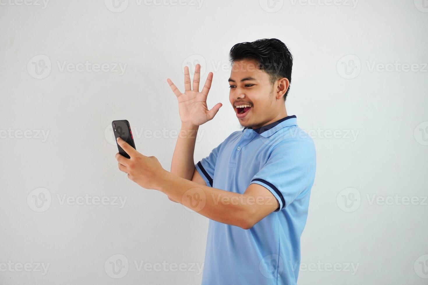 excited or happy young asian man holding phone and opened his palms wearing blue polo t shirt isolated on white background photo