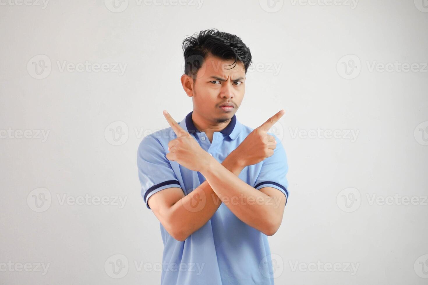Portrait of a thoughtful young asian man arms crossed with fingers pointing up wearing blue t shirt isolated on white background photo