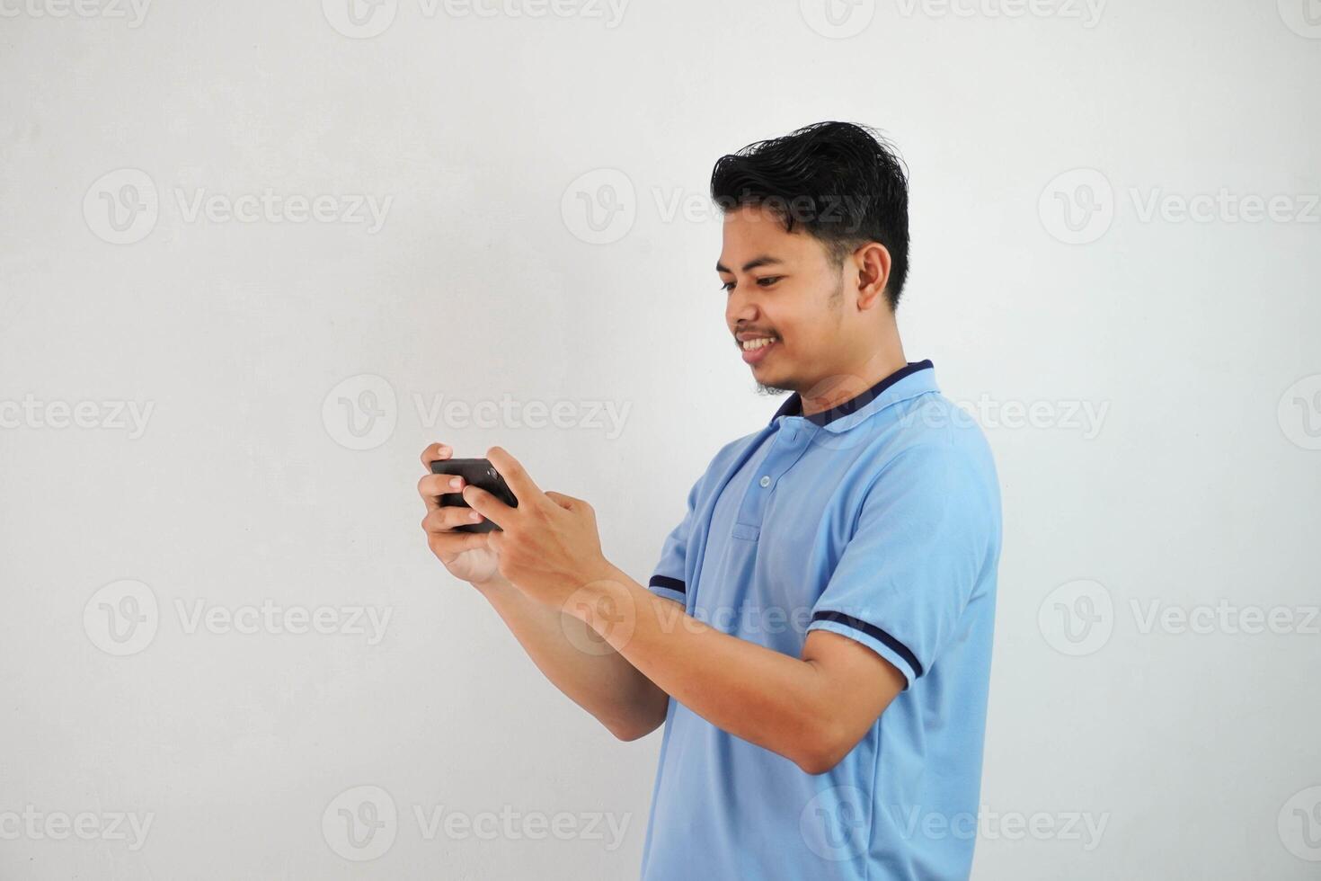 sonriente o contento retrato joven asiático hombre jugando juego con teléfono inteligente aislado en blanco antecedentes foto