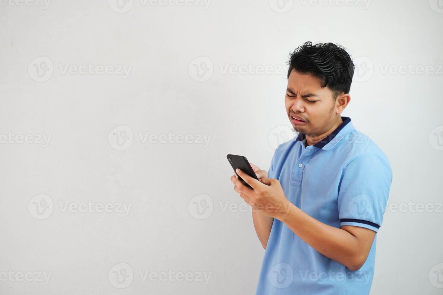 sad face with holding phone young asian man wearing blue polo t shirt isolated on white background. irritated face expressions photo