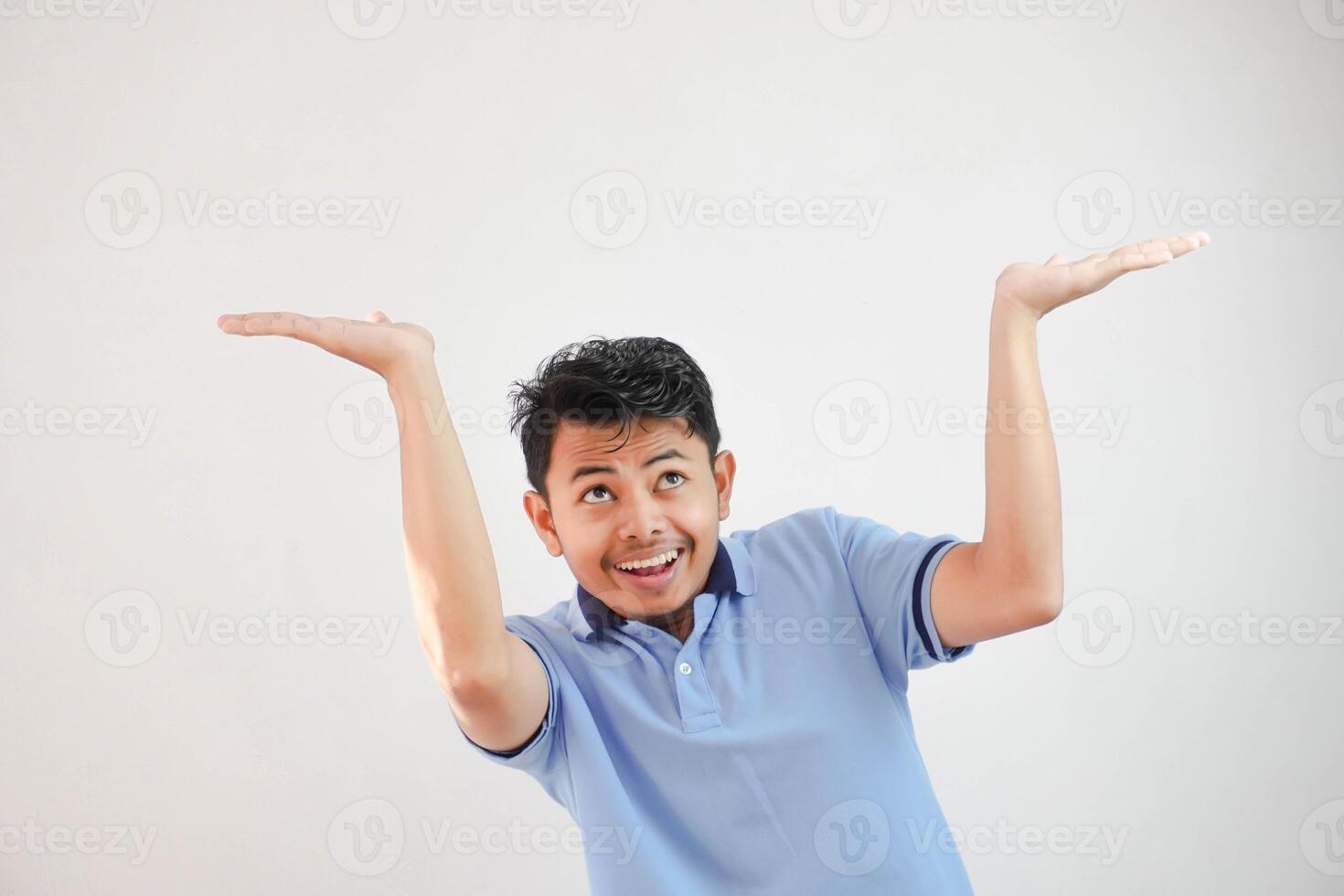 joven asiático hombre interino me gusta él es participación arriba alguna cosa pesado, pero es sólo vacío Copiar espacio vistiendo azul t camisa aislado en blanco antecedentes. conmocionado cara foto