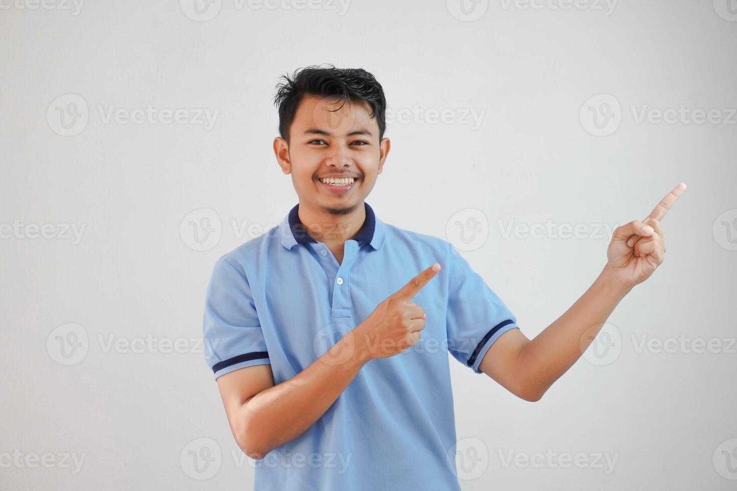 smiling asian man with fingers pointing to the side wearing blue t shirt isolated on white background photo