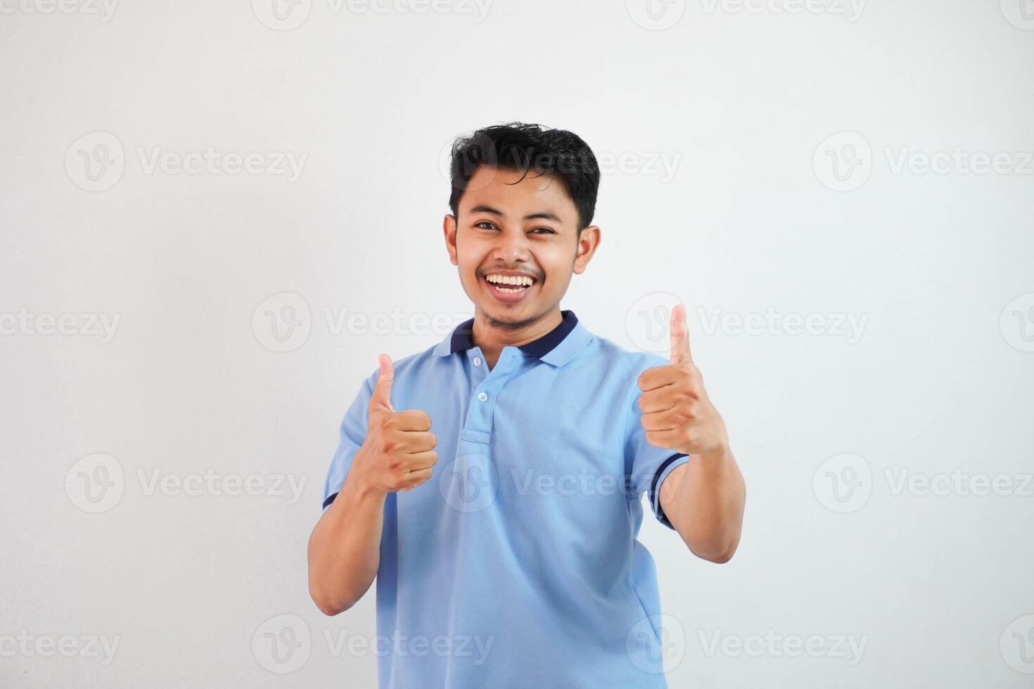 Portrait of cheerful asian man in wearing blue t shirt smiling and showing thumbs up at camera isolated over white background photo