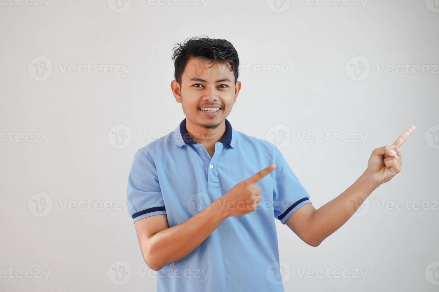 smiling asian man with fingers pointing to the side wearing blue t shirt isolated on white background photo