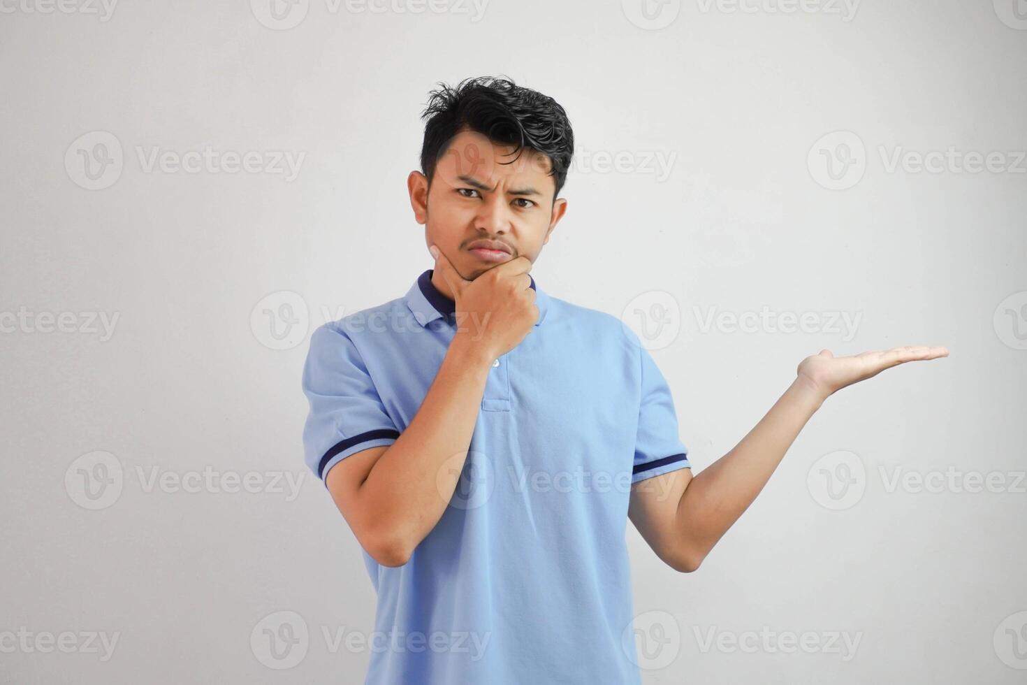 serious face asian man with an open hand the side and while holding the chin wearing blue t shirt isolated on white background photo