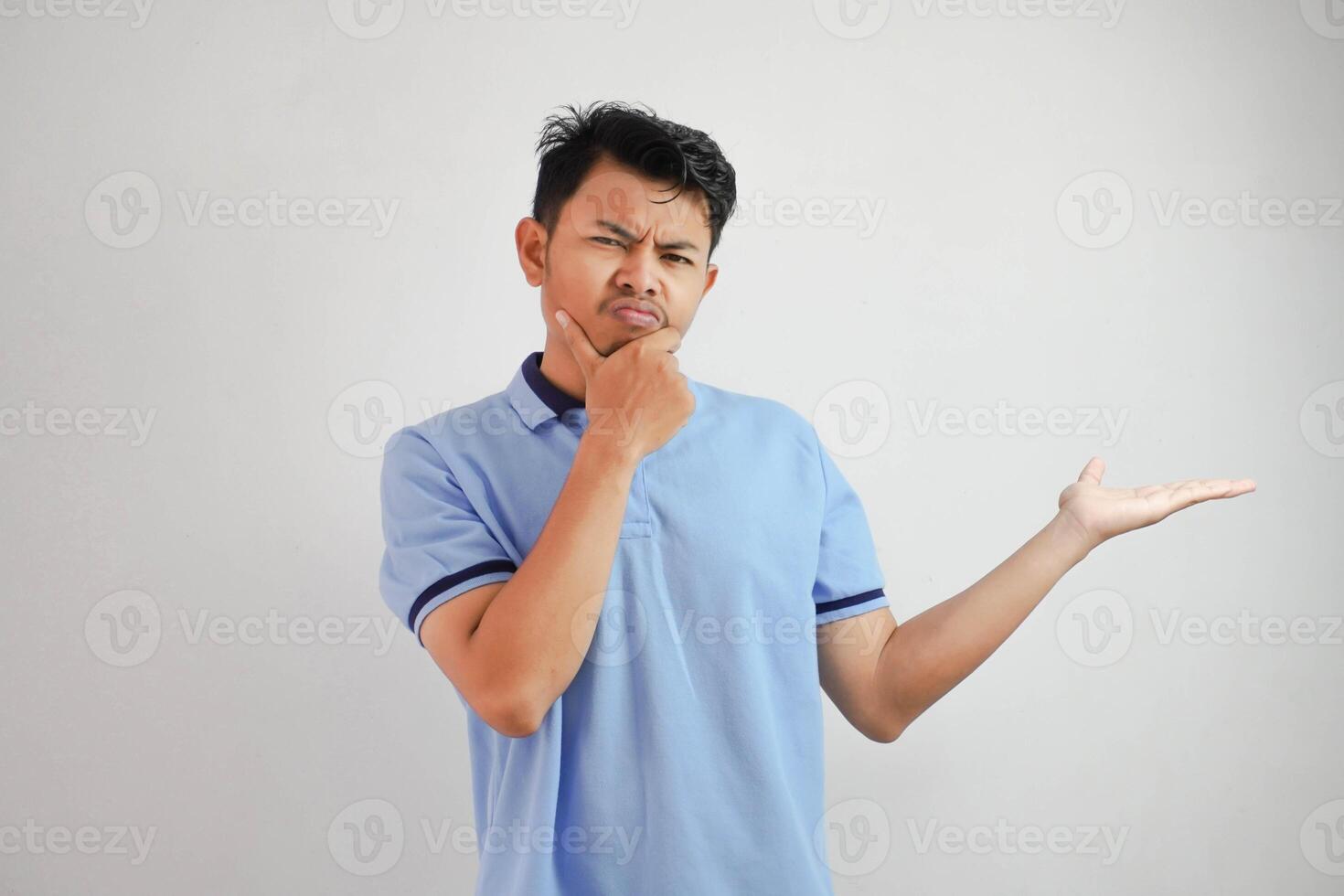 grave cara asiático hombre con un abierto mano el lado y mientras participación el barbilla vistiendo azul t camisa aislado en blanco antecedentes foto