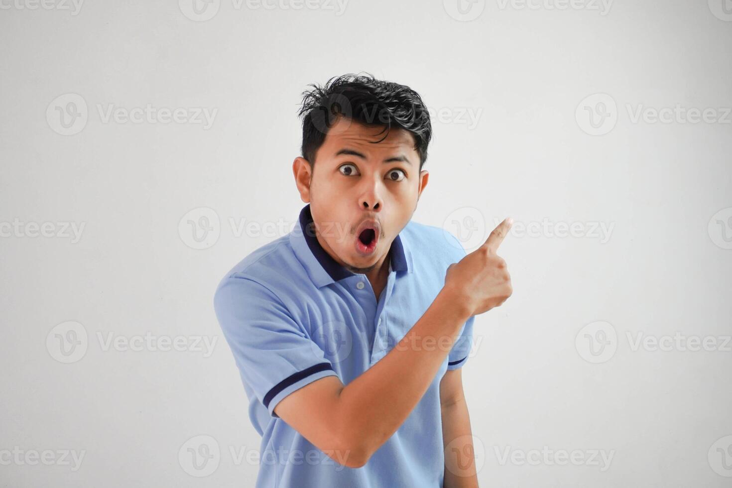 shocked asian man with an open mouth with fingers pointing to the side wearing blue t shirt isolated on white background photo