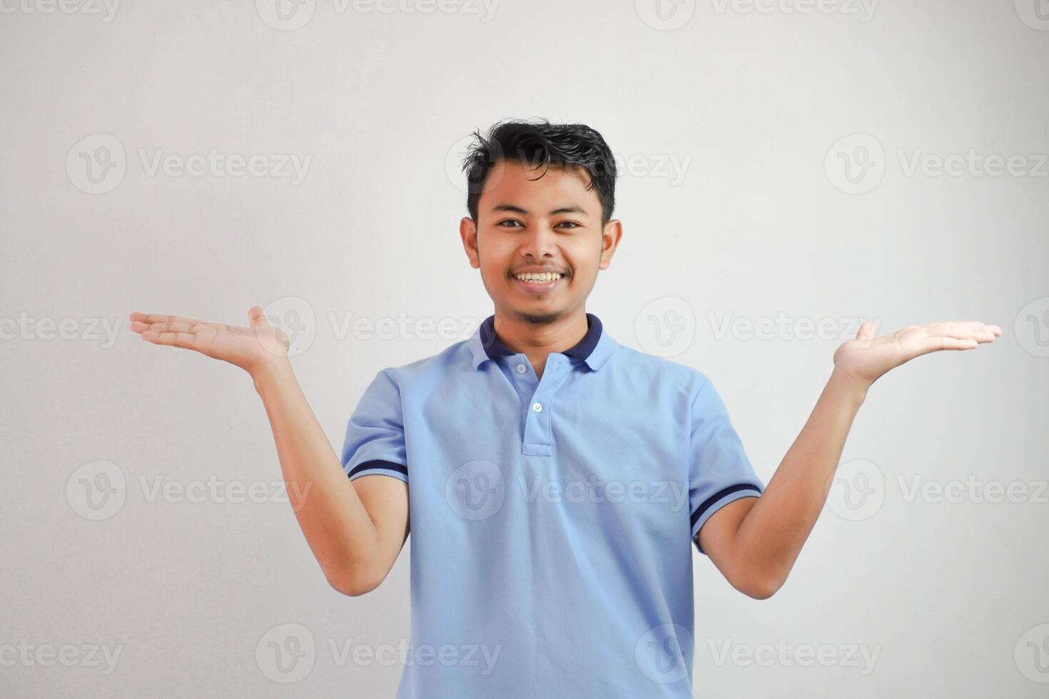 smiling asian man with both arms open at empty space beside him wearing blue t shirt isolated on white background photo