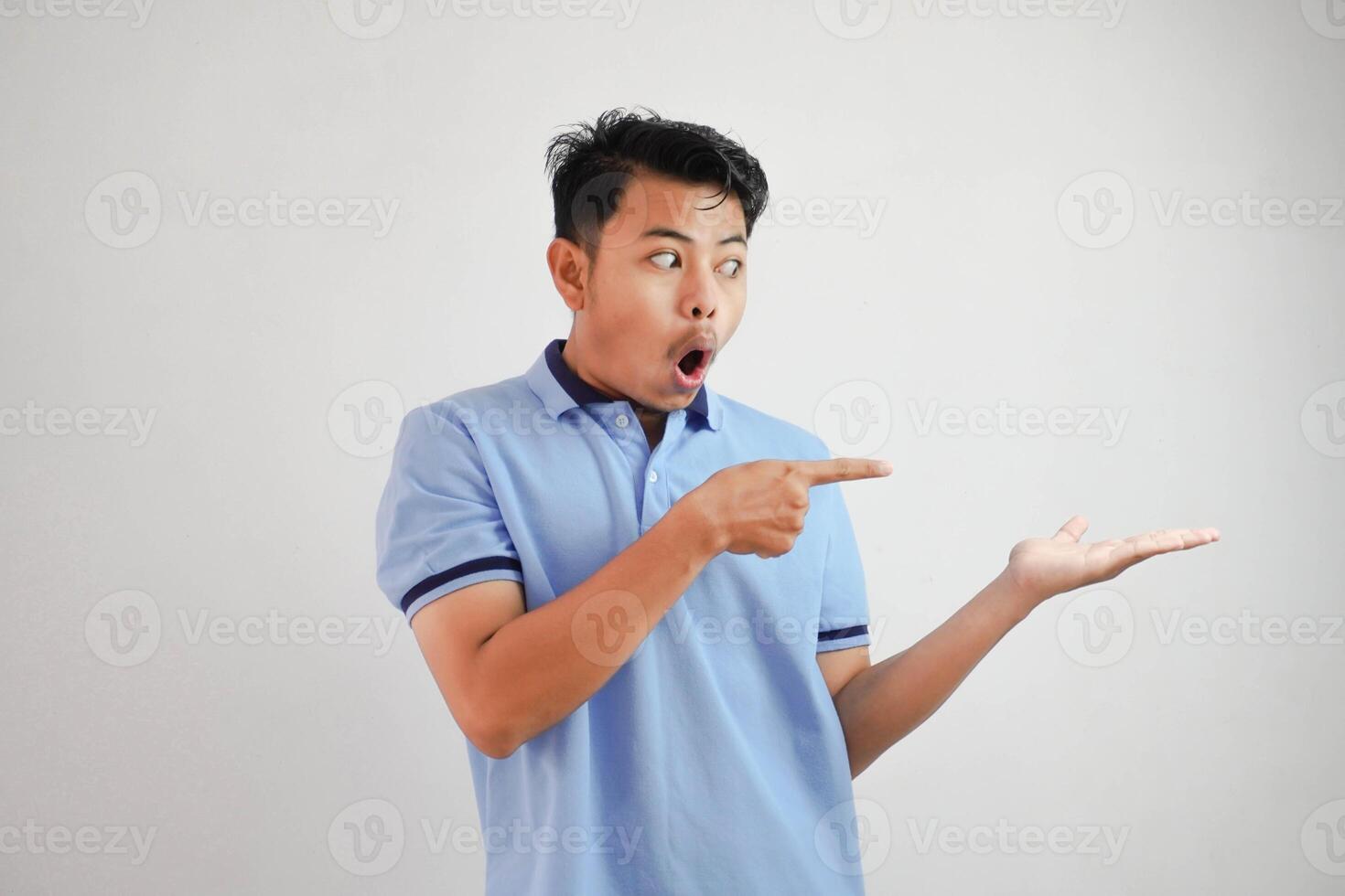 shocked asian man with an open hand with fingers pointing to the side wearing blue t shirt isolated on white background photo