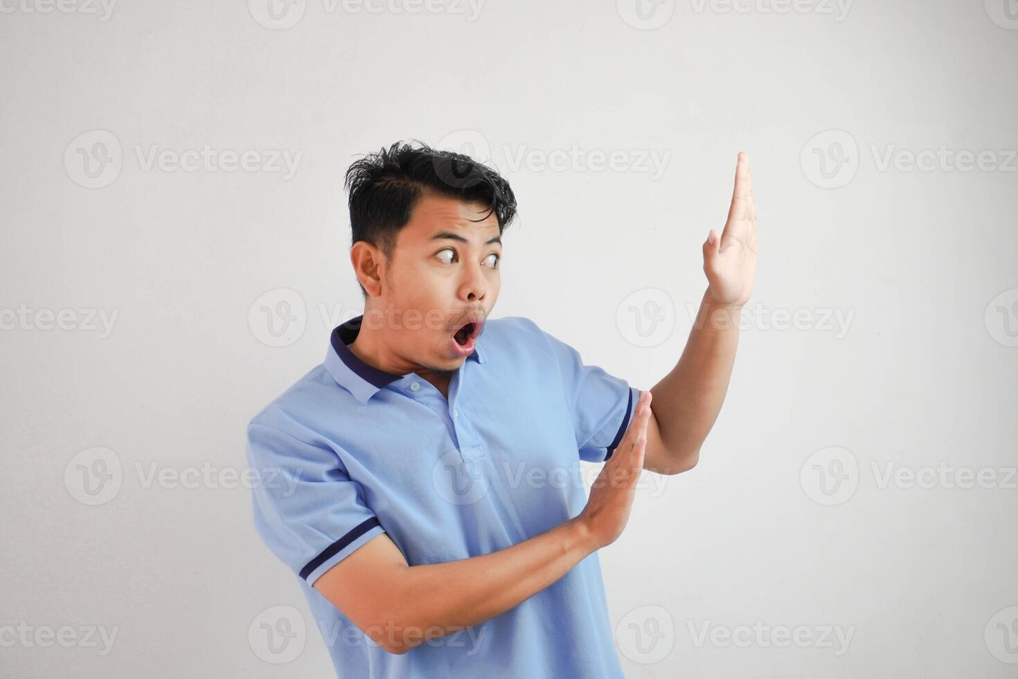 young asian man acting like he's holding side something heavy, but it's just empty copy space wearing blue t shirt isolated on white background. shocked face photo