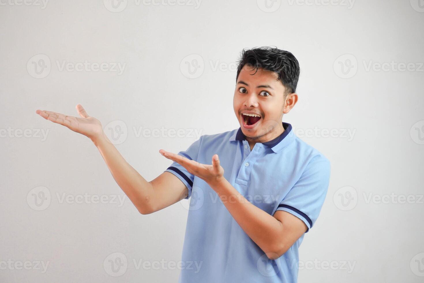 shocked asian man with an open hand with fingers pointing to the side wearing blue t shirt isolated on white background photo