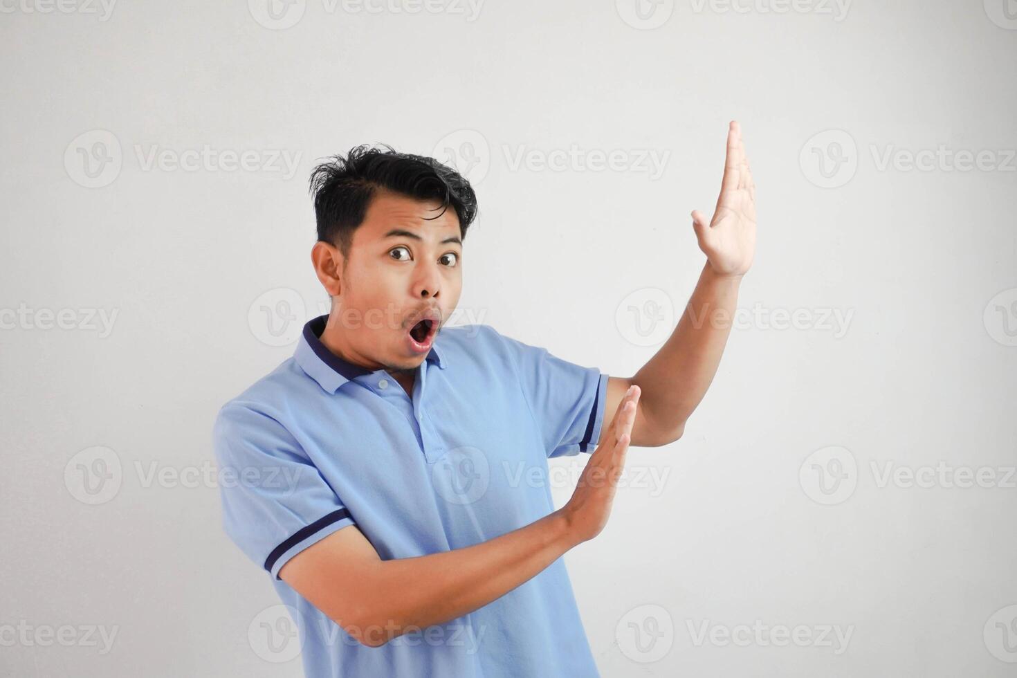 young asian man acting like he's holding side something heavy, but it's just empty copy space wearing blue t shirt isolated on white background. shocked face photo