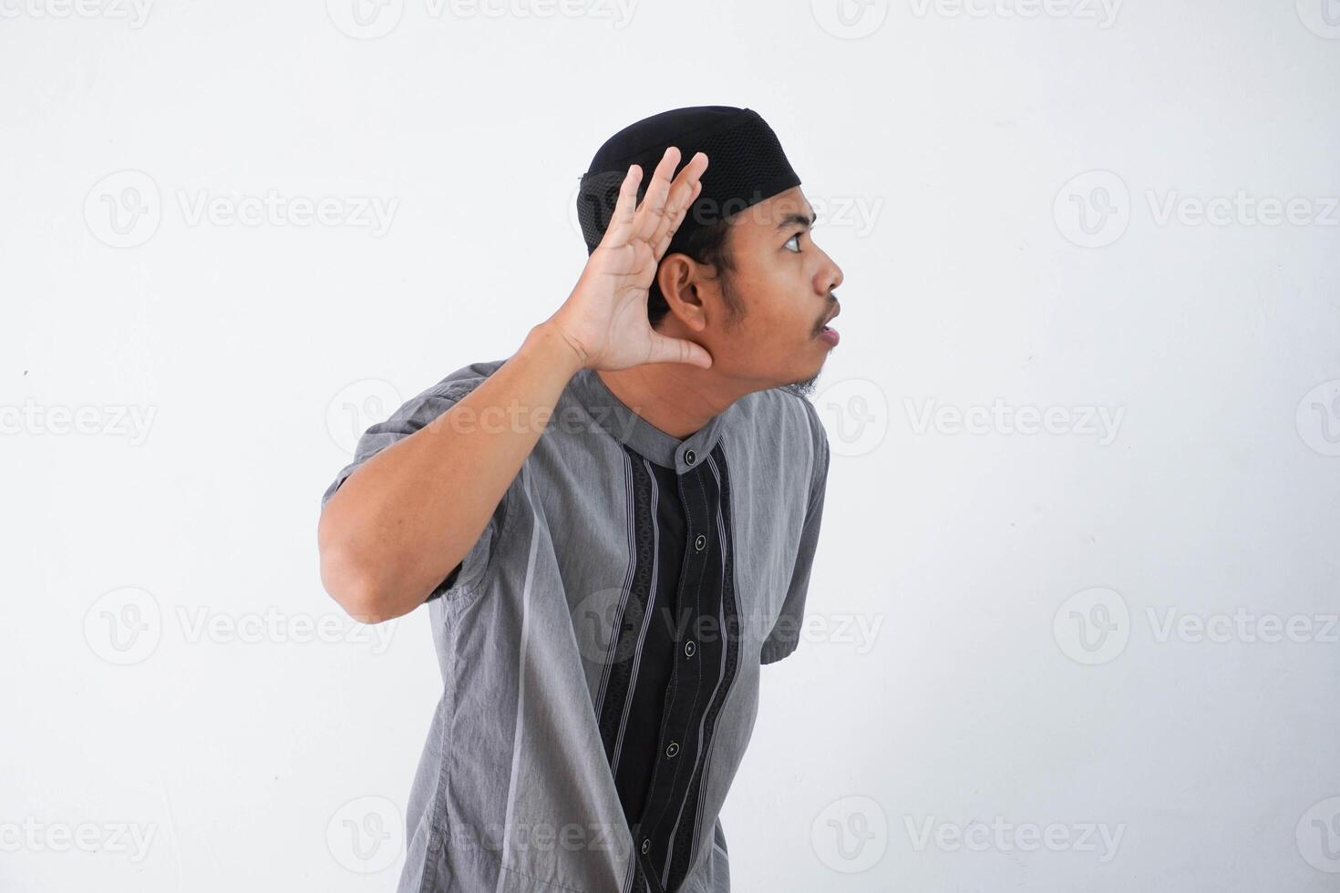 young Asian muslim man wearing grey muslim clothing, hands near ears trying to listening a gossip isolated on white background photo
