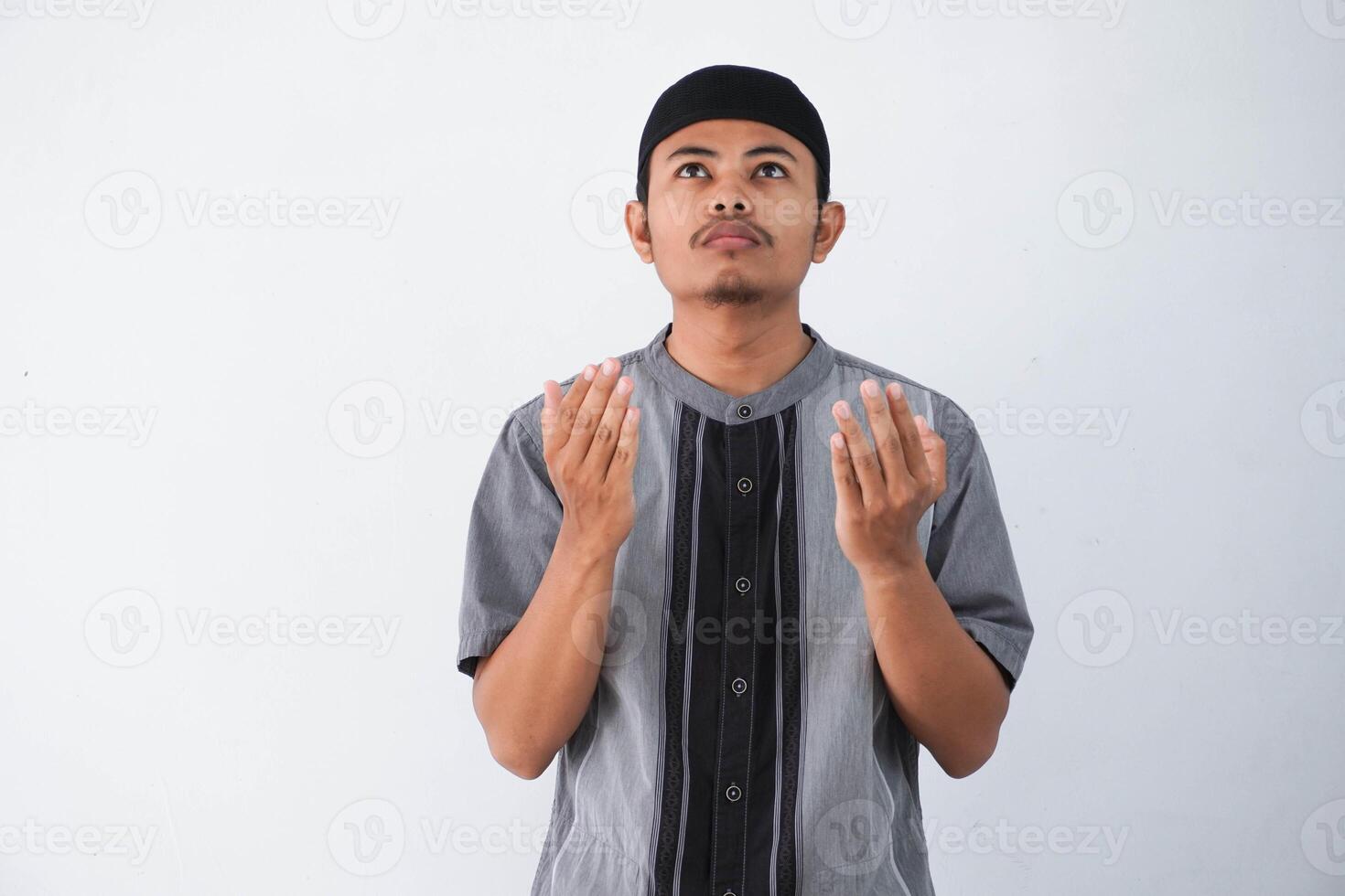 Religious young asian muslim man with open eyes praying, holding palms face up, whispering pray, isolated on white background. Religion islam, believing concept photo