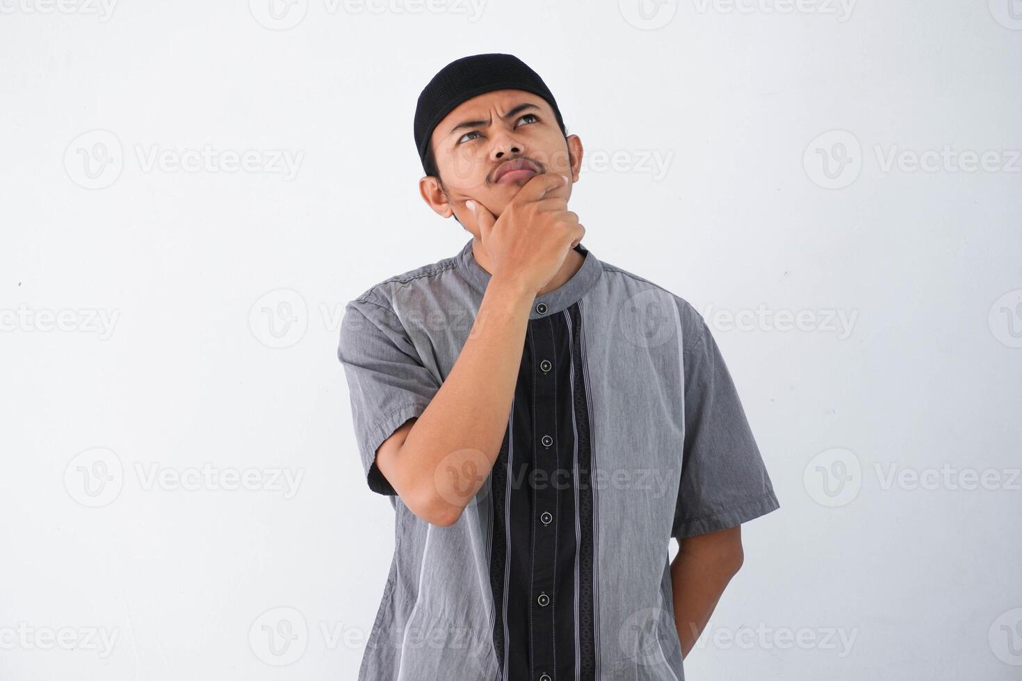 thinking young asian muslim man holding chin thinking gesture, looking for idea wearing grey muslim clothes isolated on white background photo