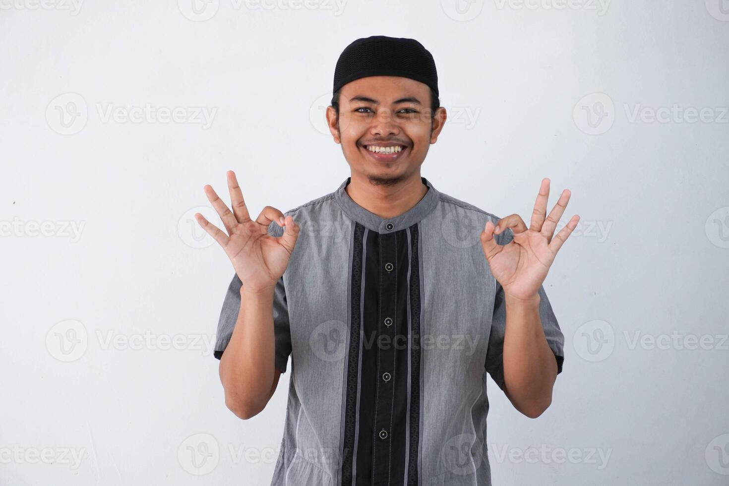 Young handsome asian muslim man smiling positive doing ok sign with hand and fingers wearing grey koko clothes isolated on white background. Successful expression. photo