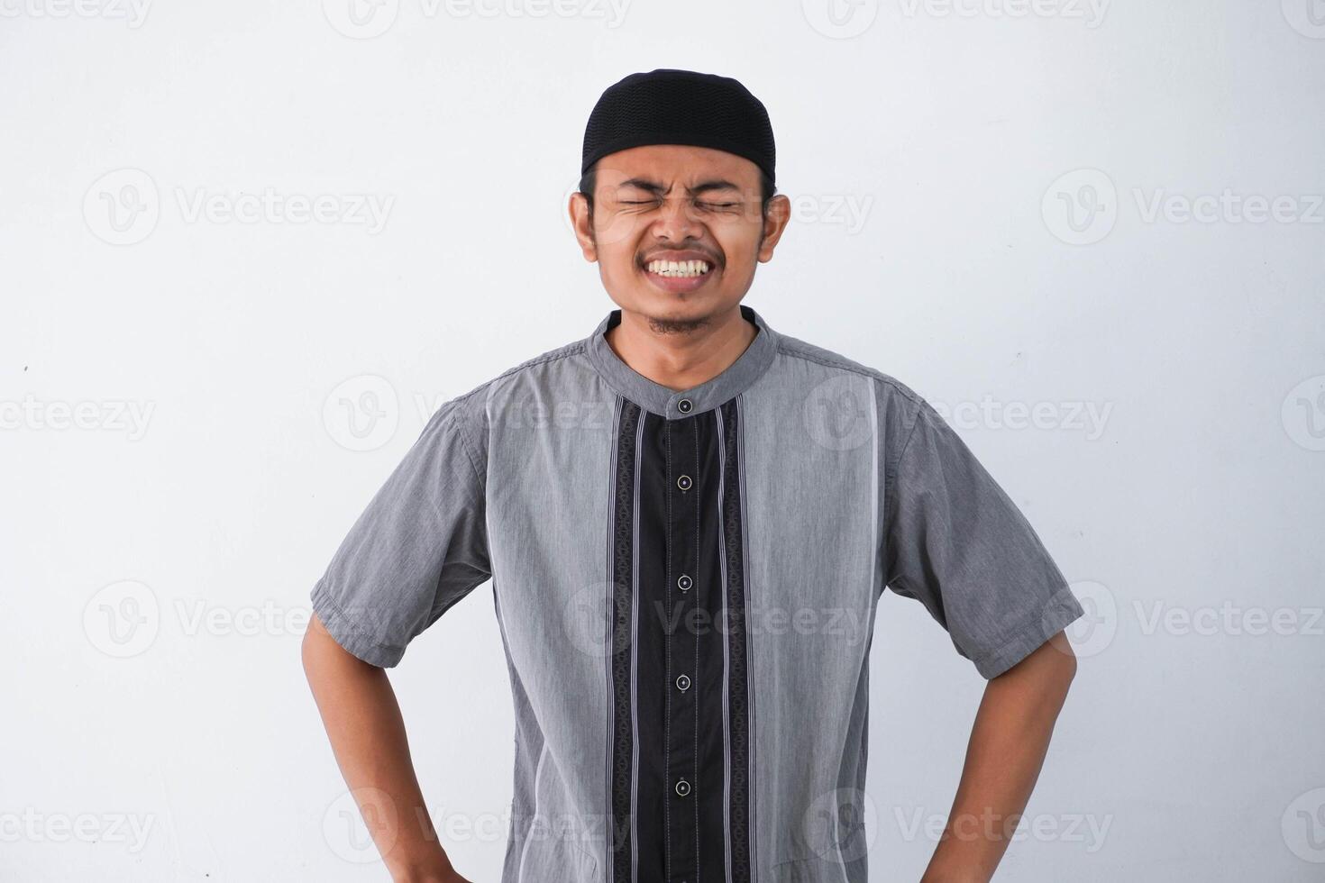 Asian muslim man feeling pain while closing his eyes and grimace wearing grey koko clothes isolated on white background photo