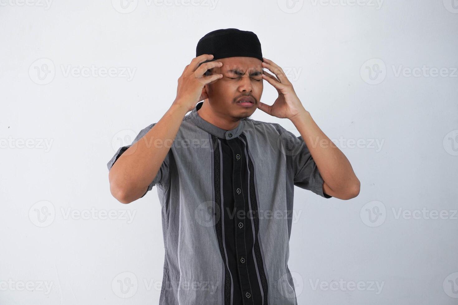 Young Asian Muslim man holding his head suffering headache wearing grey muslim clothes isolated on white background photo