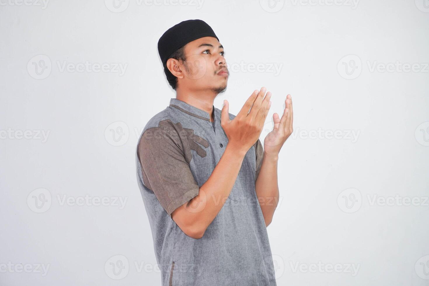 Religious young asian muslim man with open eyes praying, holding palms face up, whispering pray, isolated on white background. Religion islam, believing concept photo