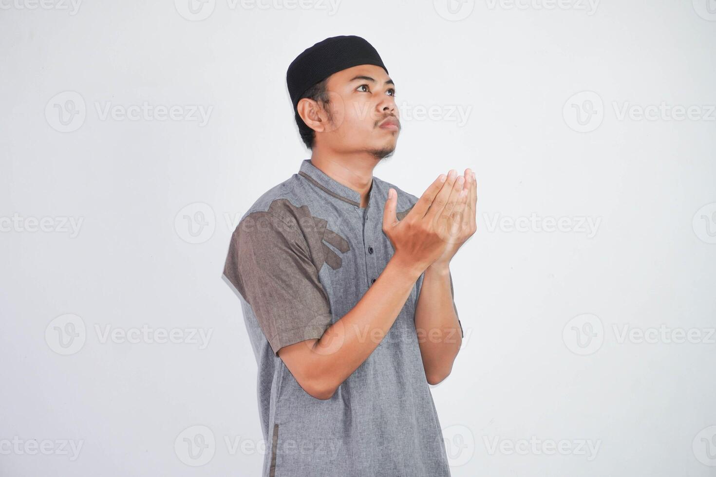 Religious young asian muslim man with open eyes praying, holding palms face up, whispering pray, isolated on white background. Religion islam, believing concept photo
