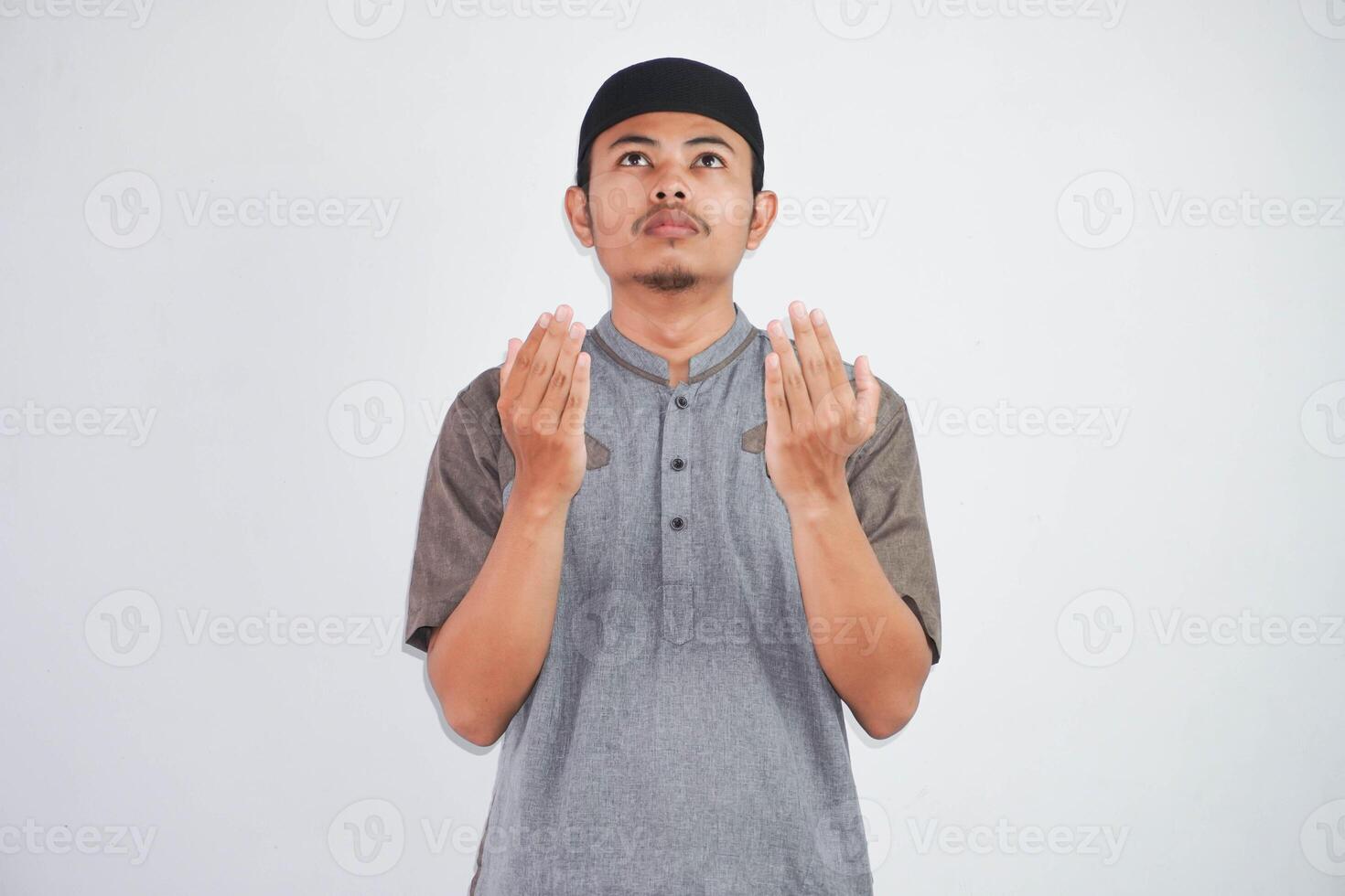 Religious young asian muslim man with open eyes praying, holding palms face up, whispering pray, isolated on white background. Religion islam, believing concept photo