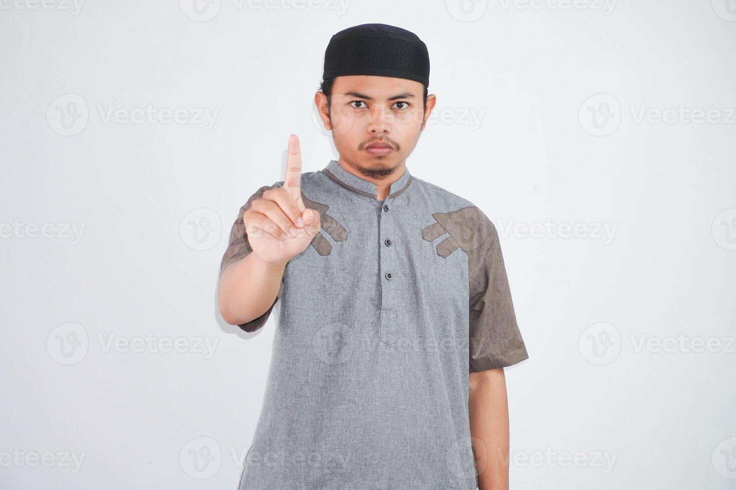 Serious young Asian Muslim man Pointing with finger up and angry expression, showing no gesture and demonstrates rejection wearing kurta clothes isolated on white background photo