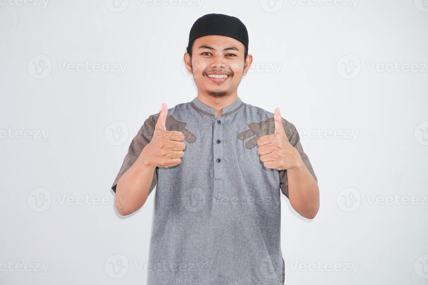 smiling or happy young muslim man showing hand thumbs up wearing grey muslim clothes isolated on white background photo