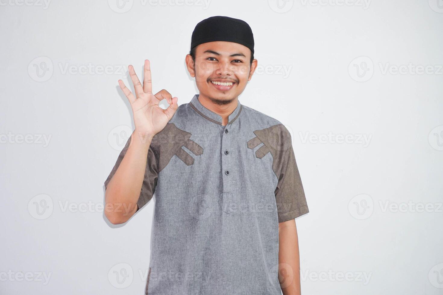 Young handsome asian muslim man smiling positive doing ok sign with hand and fingers wearing grey koko clothes isolated on white background. Successful expression. photo