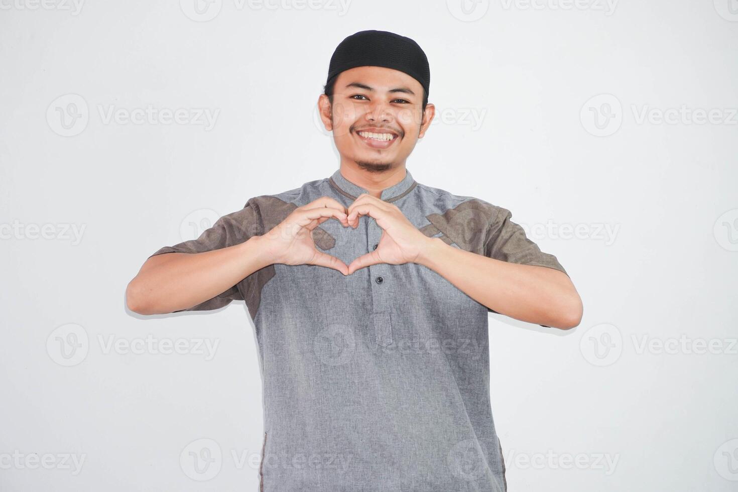 sonriente o contento joven asiático musulmán hombre demostración manos corazón gesto y mirando a cámara vistiendo musulmán ropa aislado en blanco antecedentes foto