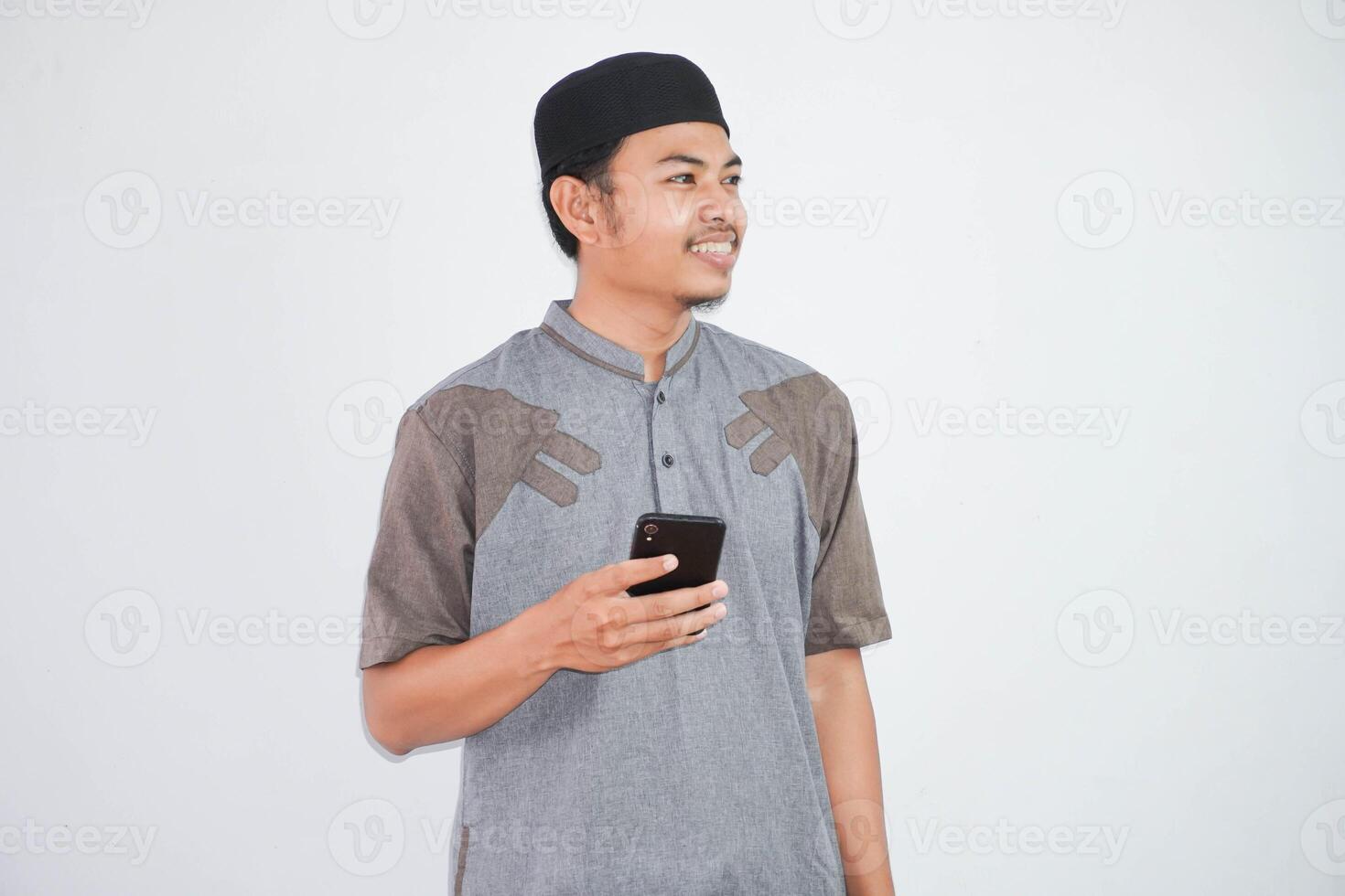 Happy or smiling young asian muslim man holding phone cellular wearing koko clothes isolated on white background. Ramadan concept photo
