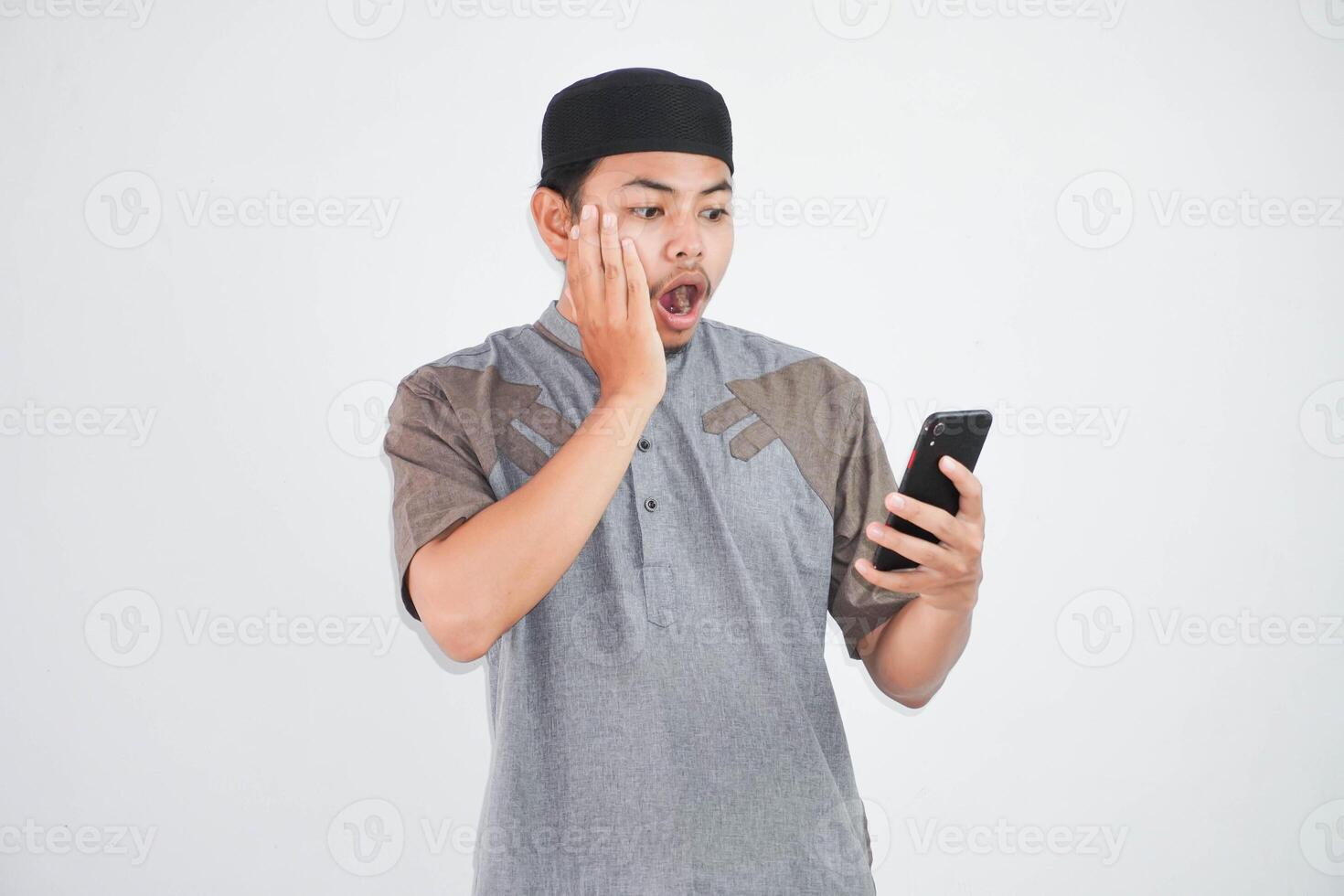 shocked young Asian Muslim man using a mobile phone, received good news wearing grey muslim clothes isolated on white background photo