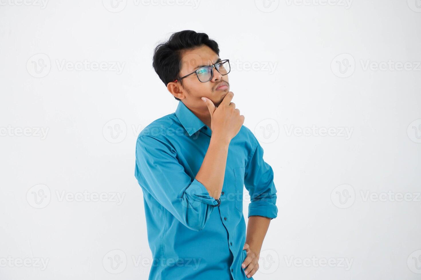 young handsome asian man with glasses thinking and looking for ideas while holding the chin wearing blue shirt isolated on white background photo