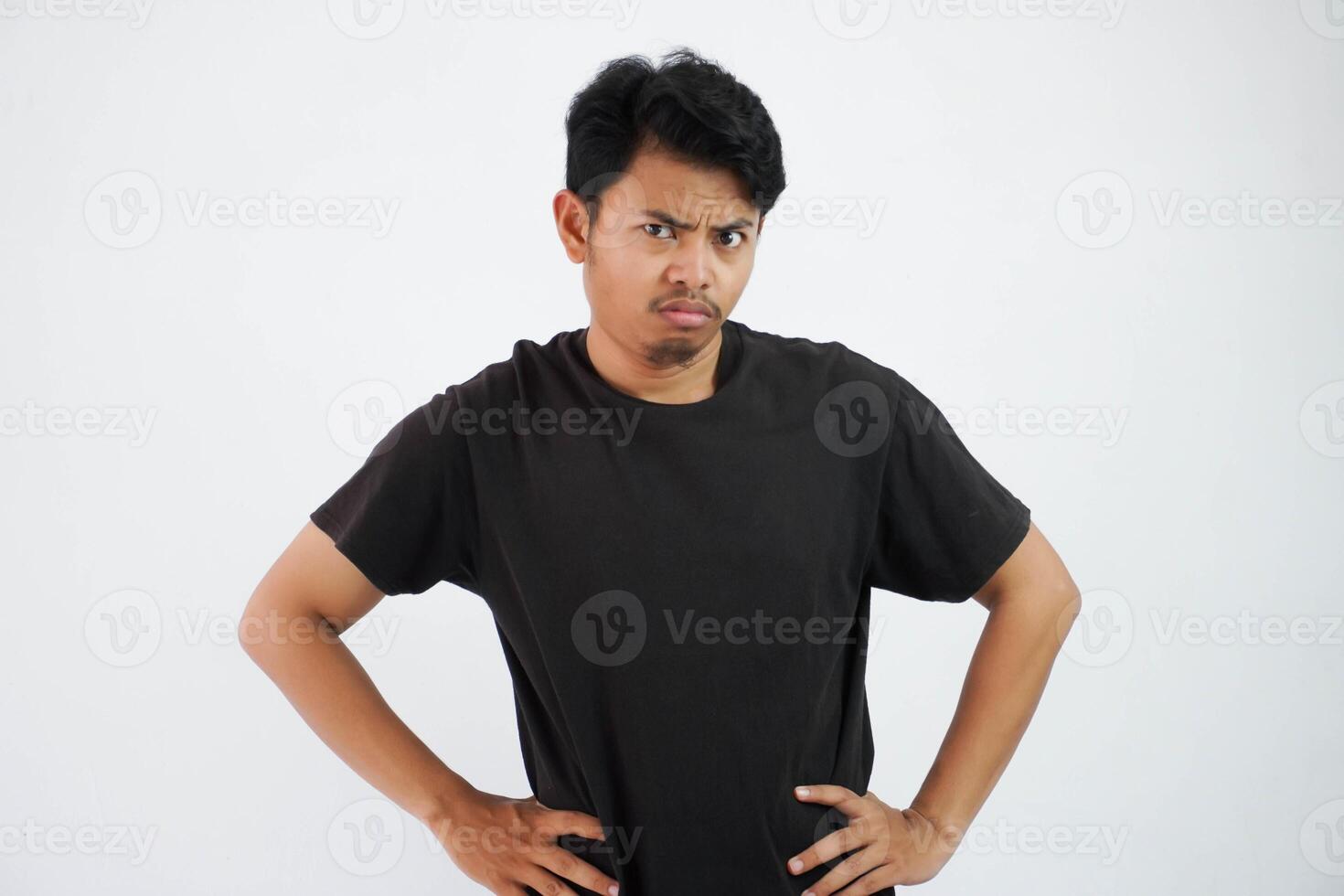 joven asiático hombre vistiendo negro t camisa estar manos a cintura siente duda a cara aislado en blanco antecedentes foto