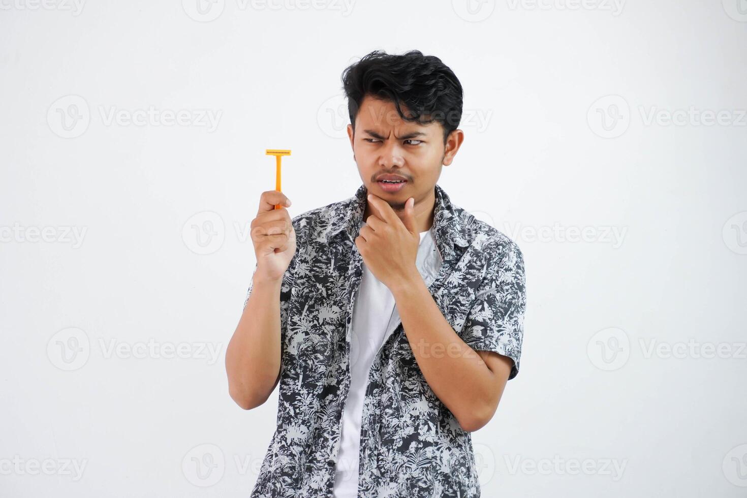 confused or amazed young asian man holding chin and looking at shaving in his hand and thinking something isolated on white background photo