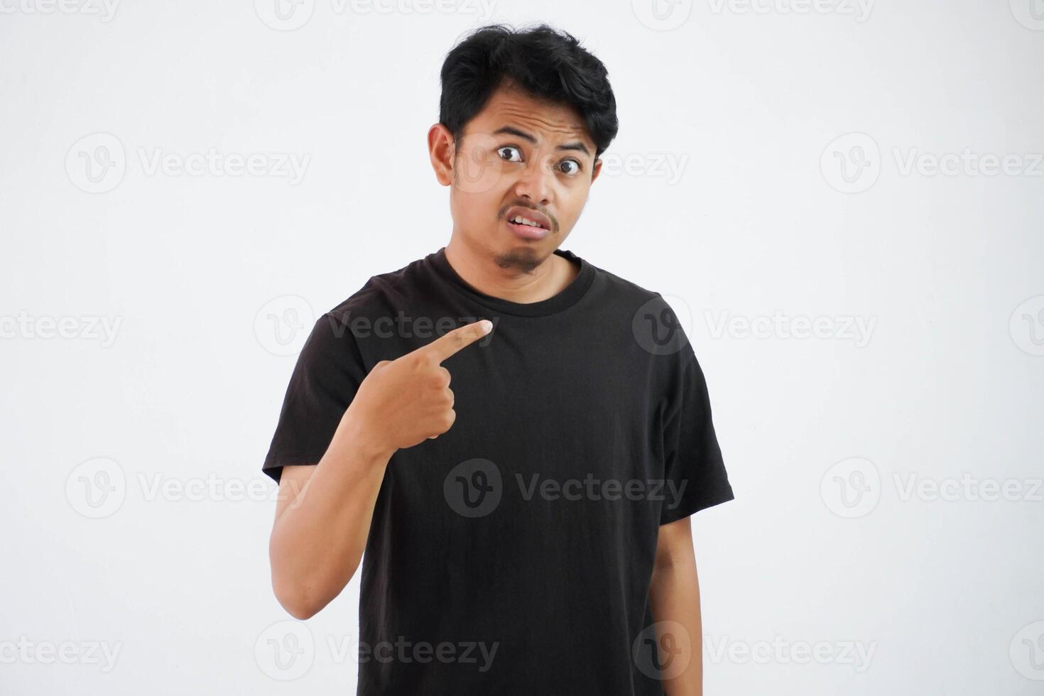 young Asian man wearing black t shirt pointing himself with unhappy displeased expression as if he confused to be accused and asking who me isolated photo