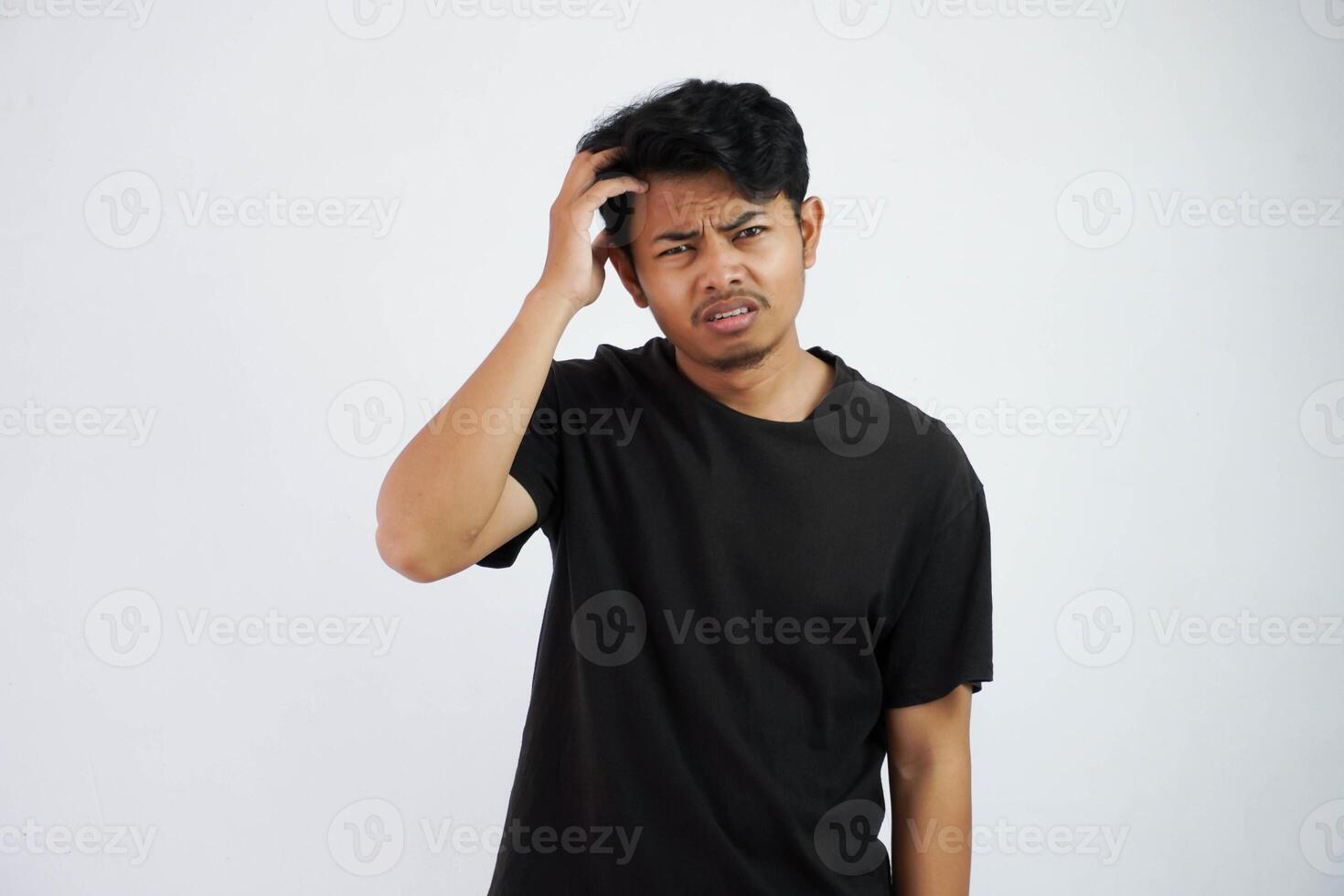 confuso joven asiático hombre participación cabeza vistiendo negro t camisa aislado en blanco antecedentes foto