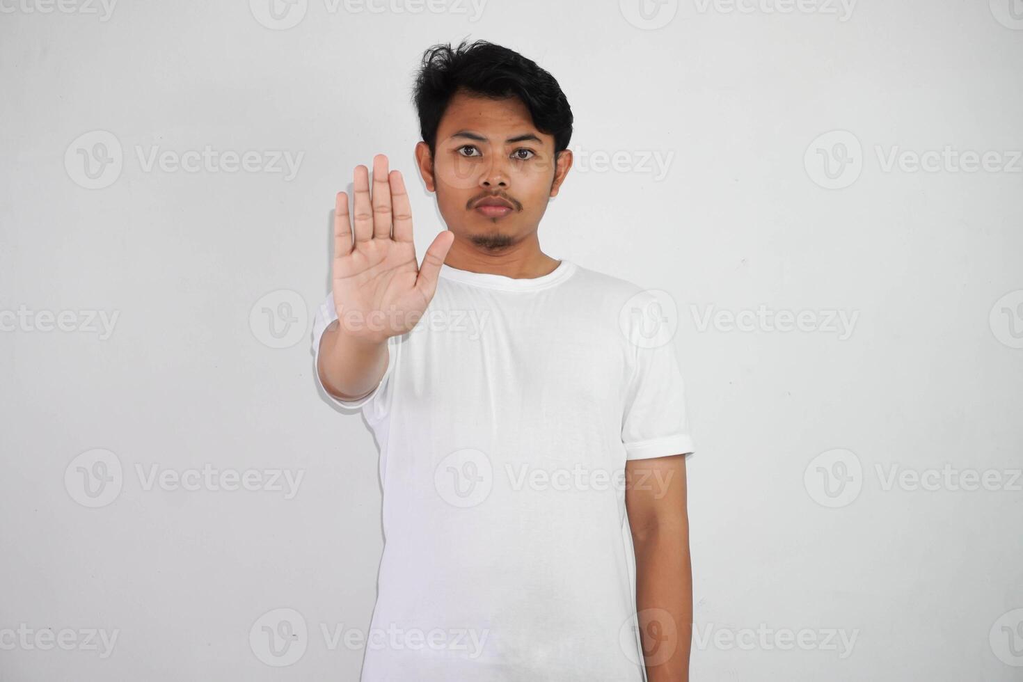 grave joven asiático hombre demostración detener gesto, demostrando negación firmar vistiendo blanco t camisa aislado en blanco antecedentes foto